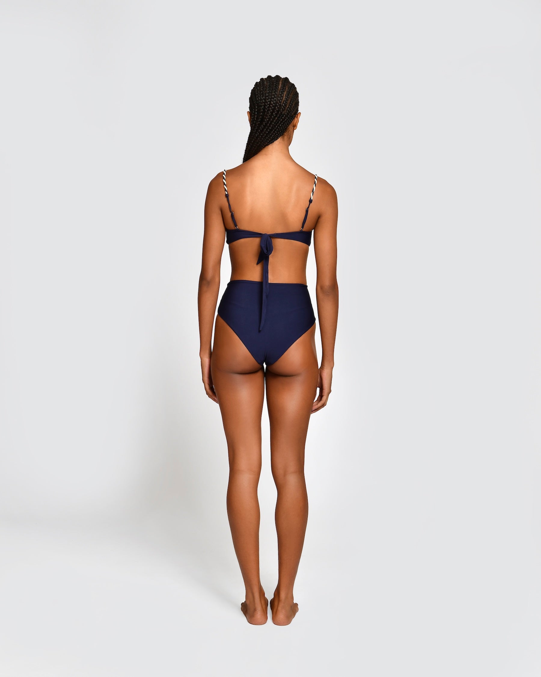 Woman wearing a navy blue bikini with thin straps and high waisted bottoms on a white background