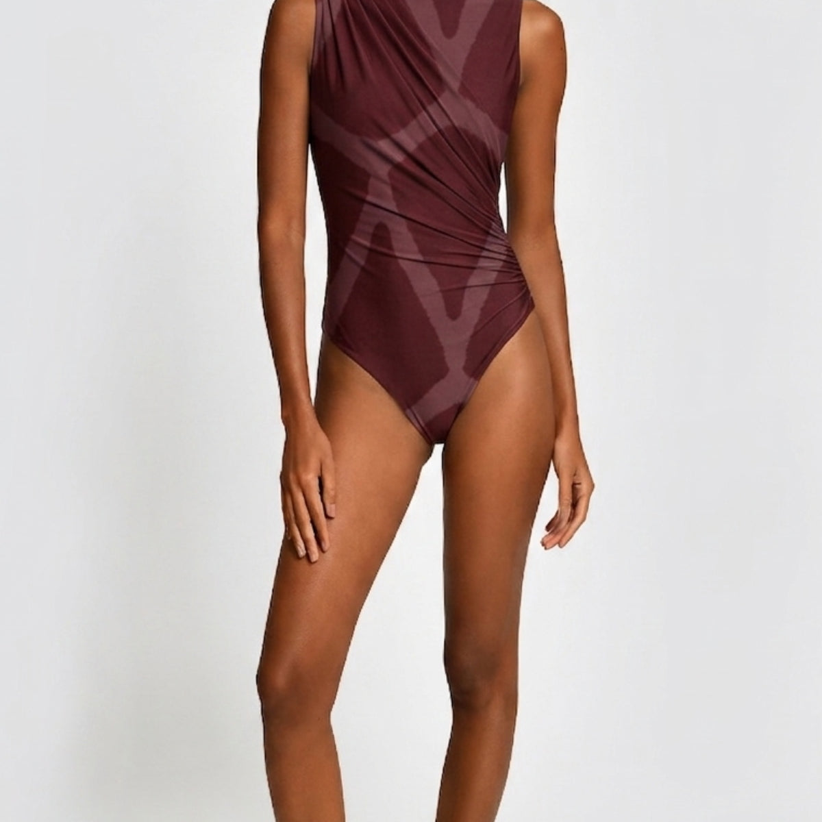 A model wearing a sleeveless, high-neck one-piece swimsuit in a deep burgundy color with a tonal geometric pattern, set against a plain light gray background.