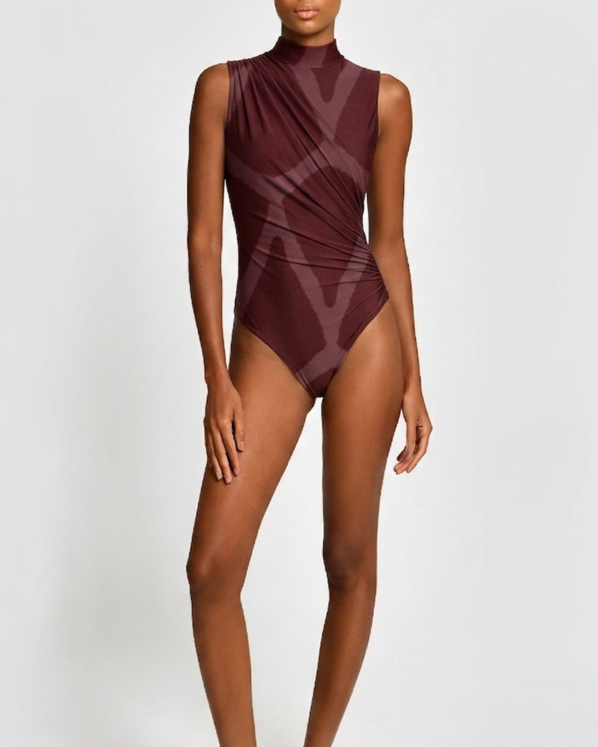 A model wearing a sleeveless, high-neck one-piece swimsuit in a deep burgundy color with a tonal geometric pattern, set against a plain light gray background.