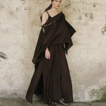 Woman wearing a dark brown dress and headscarf against a textured wall.