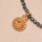 Gold beaded bracelet with a gold charm on a beige background