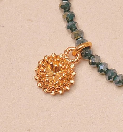Gold beaded bracelet with a gold charm on a beige background