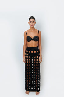 A model wearing a black laser cut Filipa skirt with an elastic waistband, designed for a comfortable fit. With a black underwire bikini top with white line detailing. 