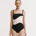 Woman wearing a black and white swimsuit with braided straps on a plain background
