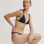 Woman wearing a navy blue bikini with beaded straps on a light gray background.