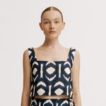 Woman wearing a navy and white patterned top on a plain background.