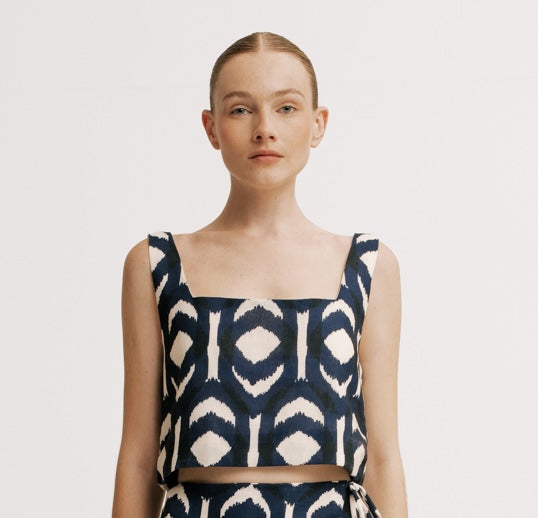 Woman wearing a navy and white patterned top on a plain background.