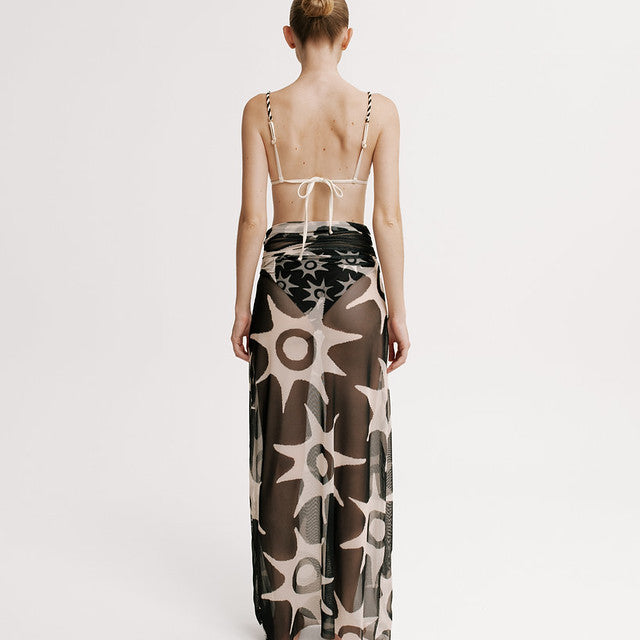 Model wearing a long, patterned dress with thin straps on a white background.