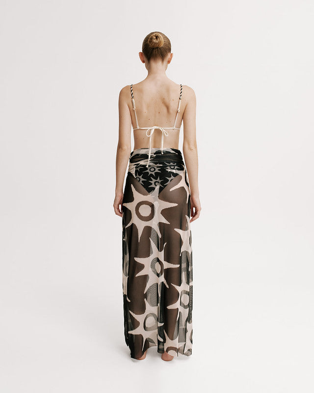 Model wearing a long, patterned dress with thin straps on a white background.