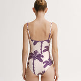 Woman wearing a one-piece swimsuit with purple palm tree pattern on a white background.