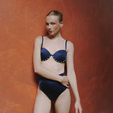 Woman wearing a blue bikini against a textured red wall.