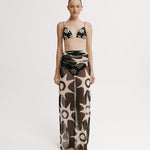 Model wearing a patterned bikini set with a long mesh skirt on a white background