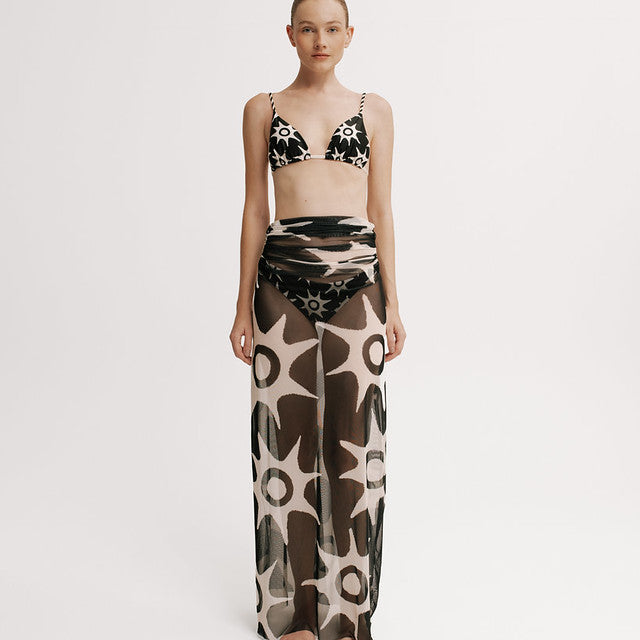 Model wearing a patterned bikini set with a long mesh skirt on a white background
