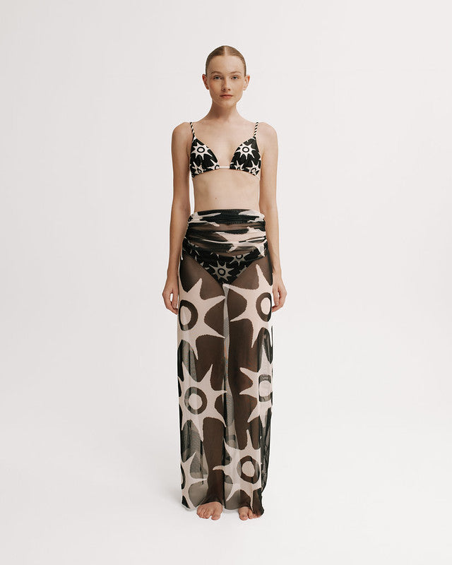 Model wearing a patterned bikini set with a long mesh skirt on a white background