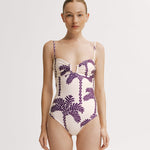 Woman wearing a one-piece swimsuit with purple palm tree pattern on a white background