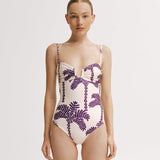 Woman wearing a one-piece swimsuit with purple palm tree pattern on a white background