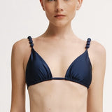 Woman wearing a navy blue bikini with thin straps on a light background.