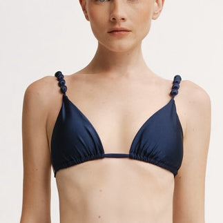 Woman wearing a navy blue bikini with thin straps on a light background.