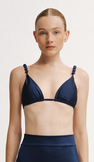 Woman wearing a navy blue bikini with thin straps on a light background.
