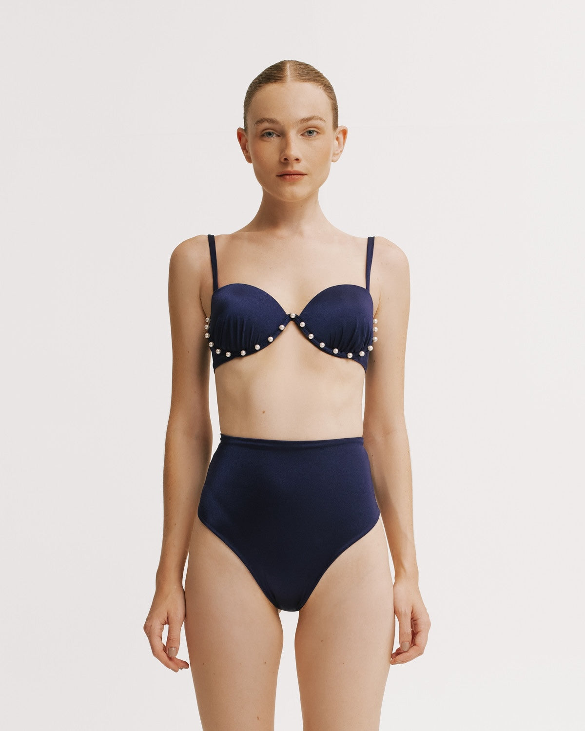 Woman wearing a navy blue bikini with polka dot details on a white background.