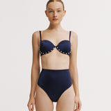 Woman wearing a navy blue bikini with polka dot details on a white background.