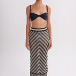 Woman wearing a black bikini top and a long, patterned skirt with fringes on a white background
