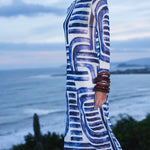 Woman wearing a blue and white patterned dress standing by the ocean.