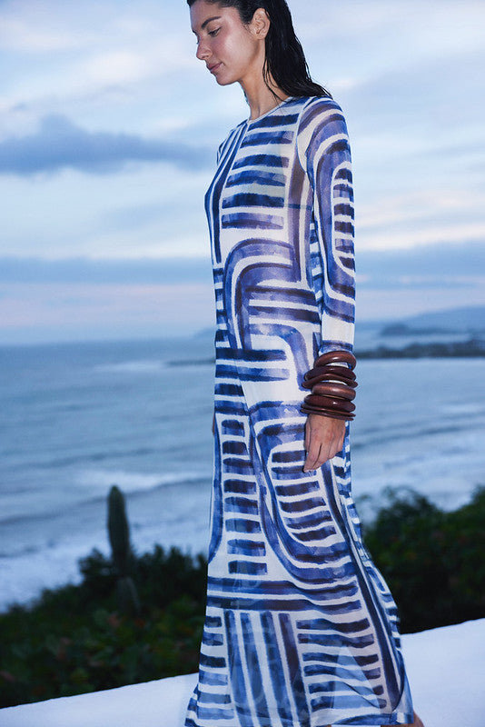 Woman wearing a blue and white patterned dress standing by the ocean.