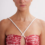 Woman wearing a red and white patterned top with thin straps against a plain background