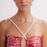 Woman wearing a red and white patterned top with thin straps against a plain background