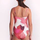 A girl wearing a one-piece swimsuit with a pink, red, and white abstract watercolor pattern against a plain white background.