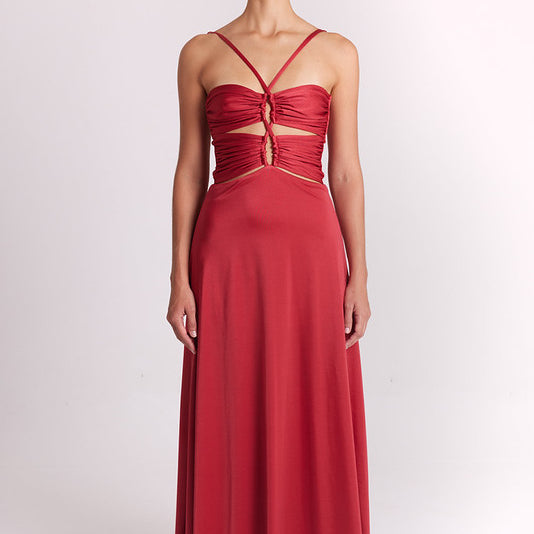 A model wearing a red strapless maxi dress with a ruched sweetheart bodice, front cutout details, and a flowing skirt, standing against a plain light gray studio background.