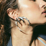Close-up of a woman wearing a set of various sized silver crescent  hoop earrings. 