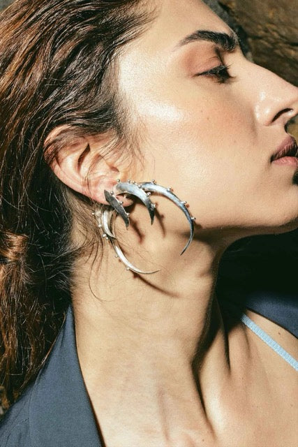 Close-up of a woman wearing a set of various sized silver crescent  hoop earrings. 