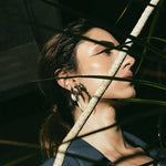 Woman with closed eyes standing among plant leaves.