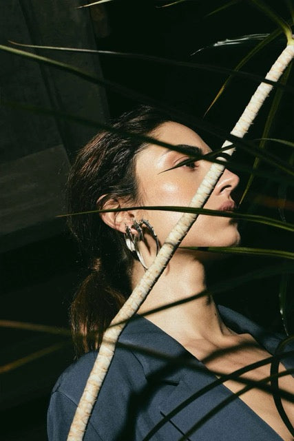 Woman with closed eyes standing among plant leaves.