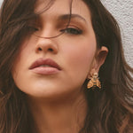 Close-up of a woman wearing a gold bee-shaped earring against a neutral background