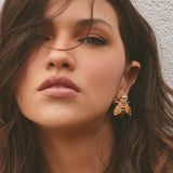 Close-up of a woman wearing a gold bee-shaped earring against a neutral background