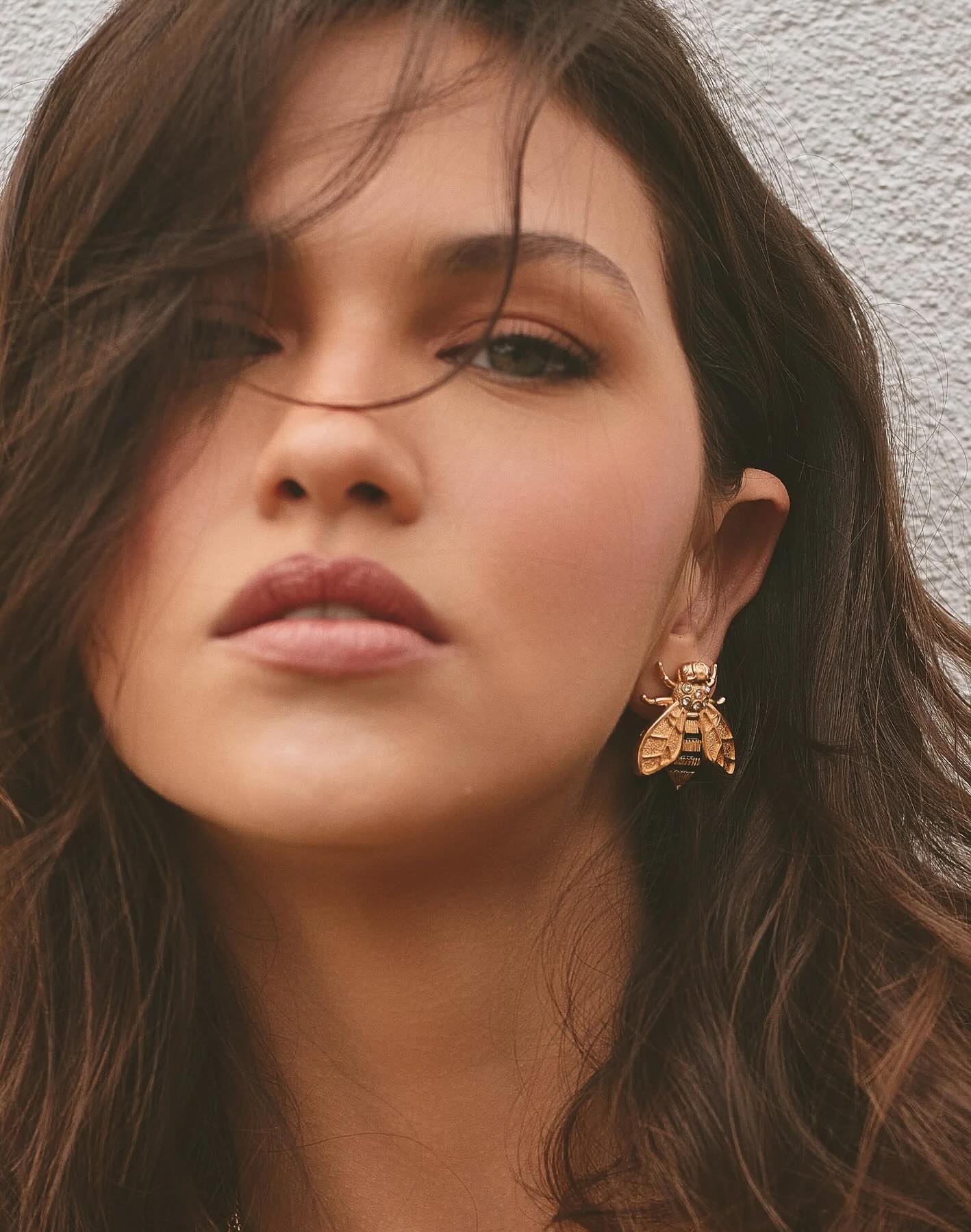 Close-up of a woman wearing a gold bee-shaped earring against a neutral background