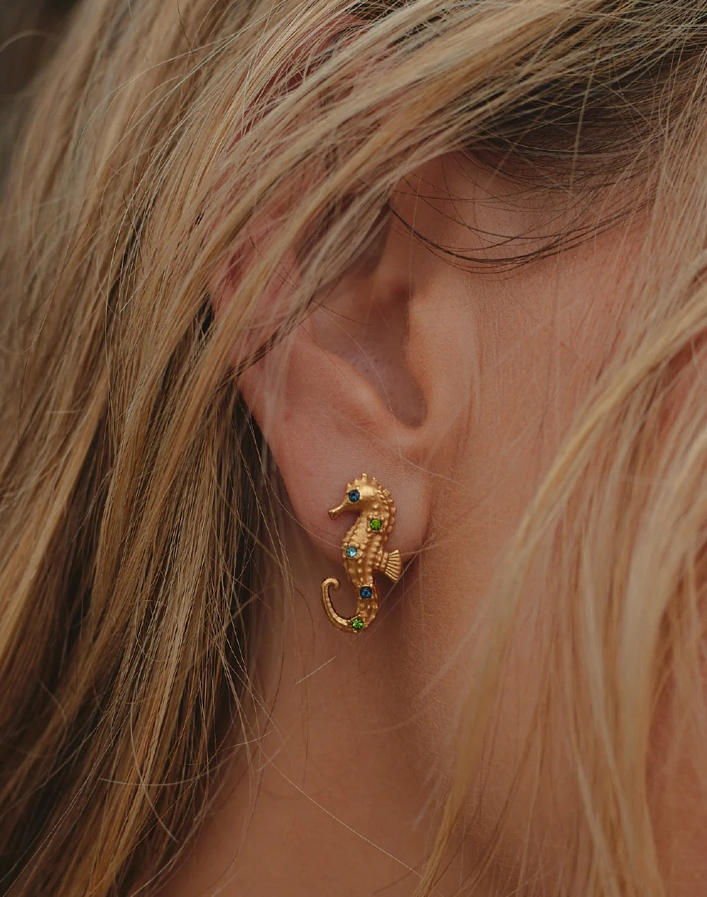 Gold seahorse earring worn by a person with blonde hair.