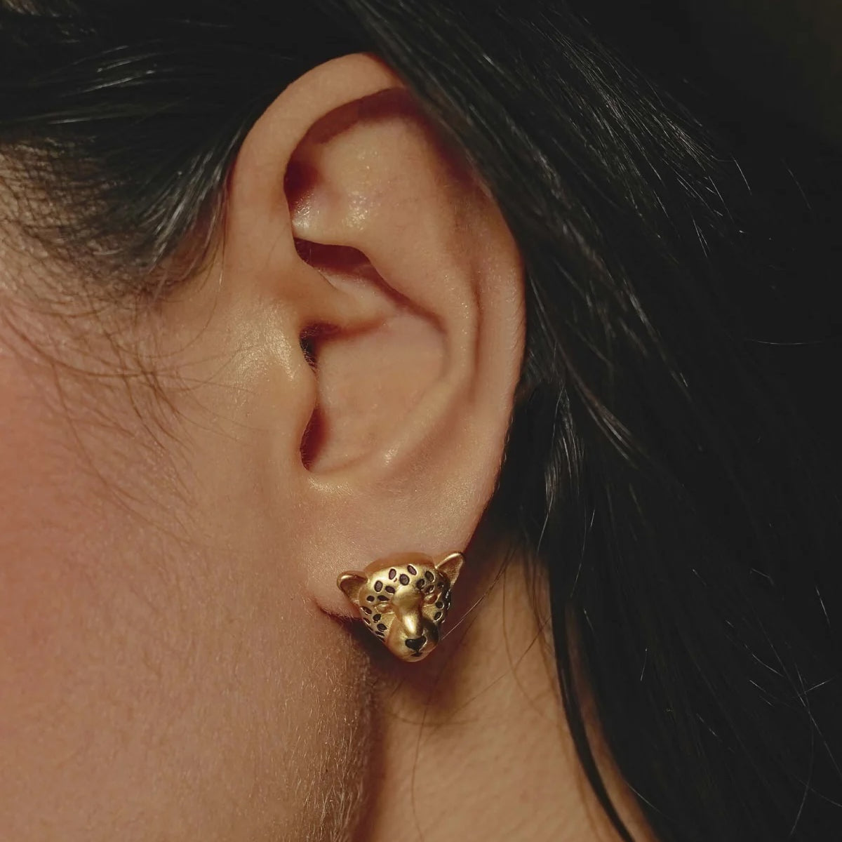 Gold leopard-shaped earring worn by a person with dark hair.