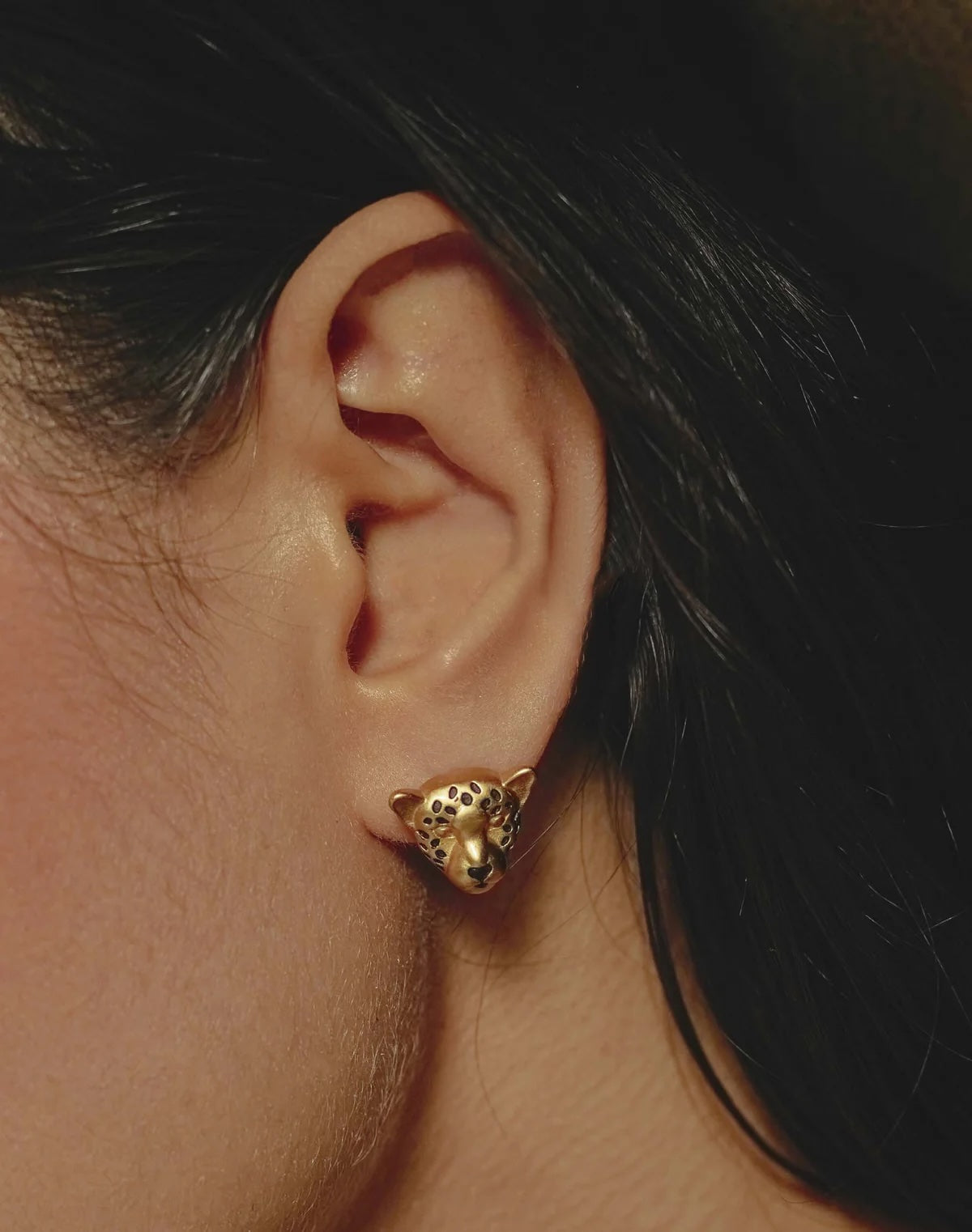 Gold leopard-shaped earring worn by a person with dark hair.