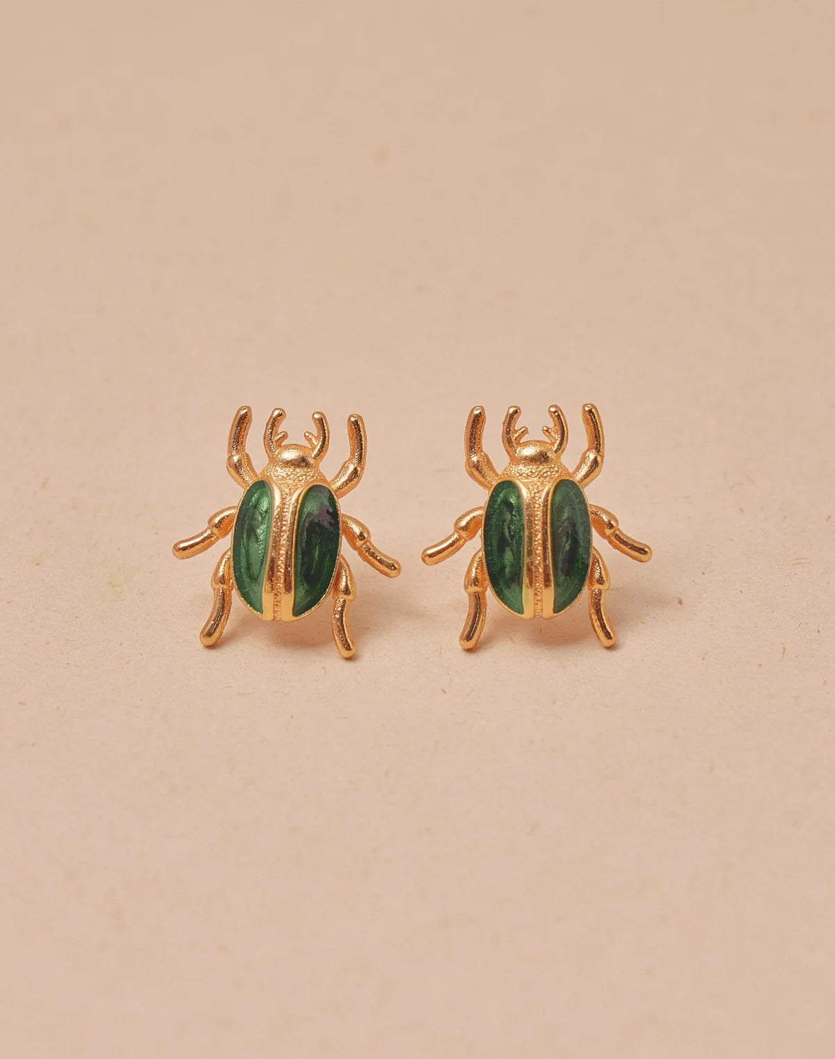 Gold beetle-shaped earrings with green accents on a beige background