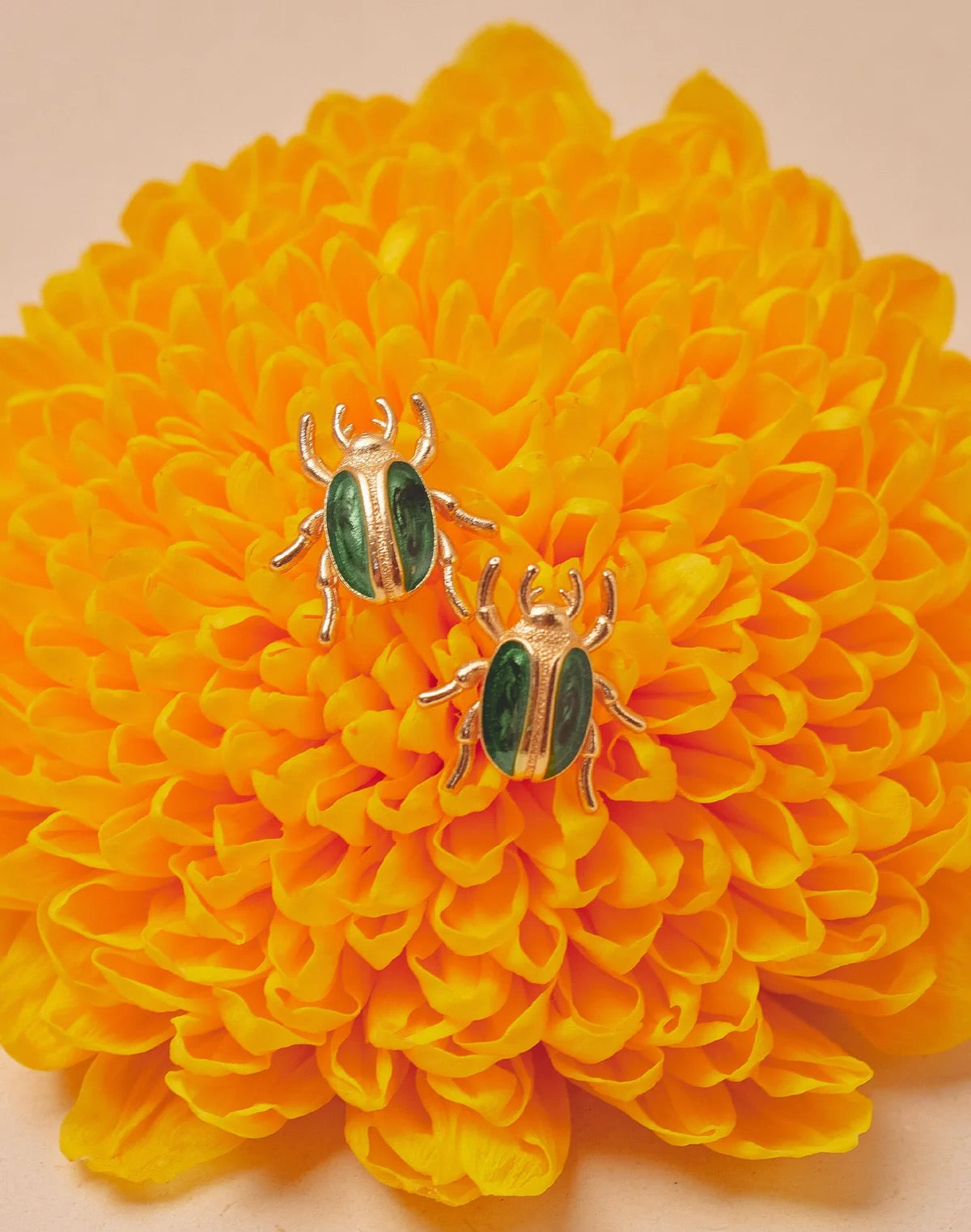 Two gold and green beetle-shaped earrings on a yellow flower.
