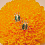 Two gold and green beetle-shaped earrings on a yellow flower.
