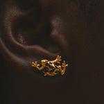Close up of gold frog-shaped earring worn on an ear.