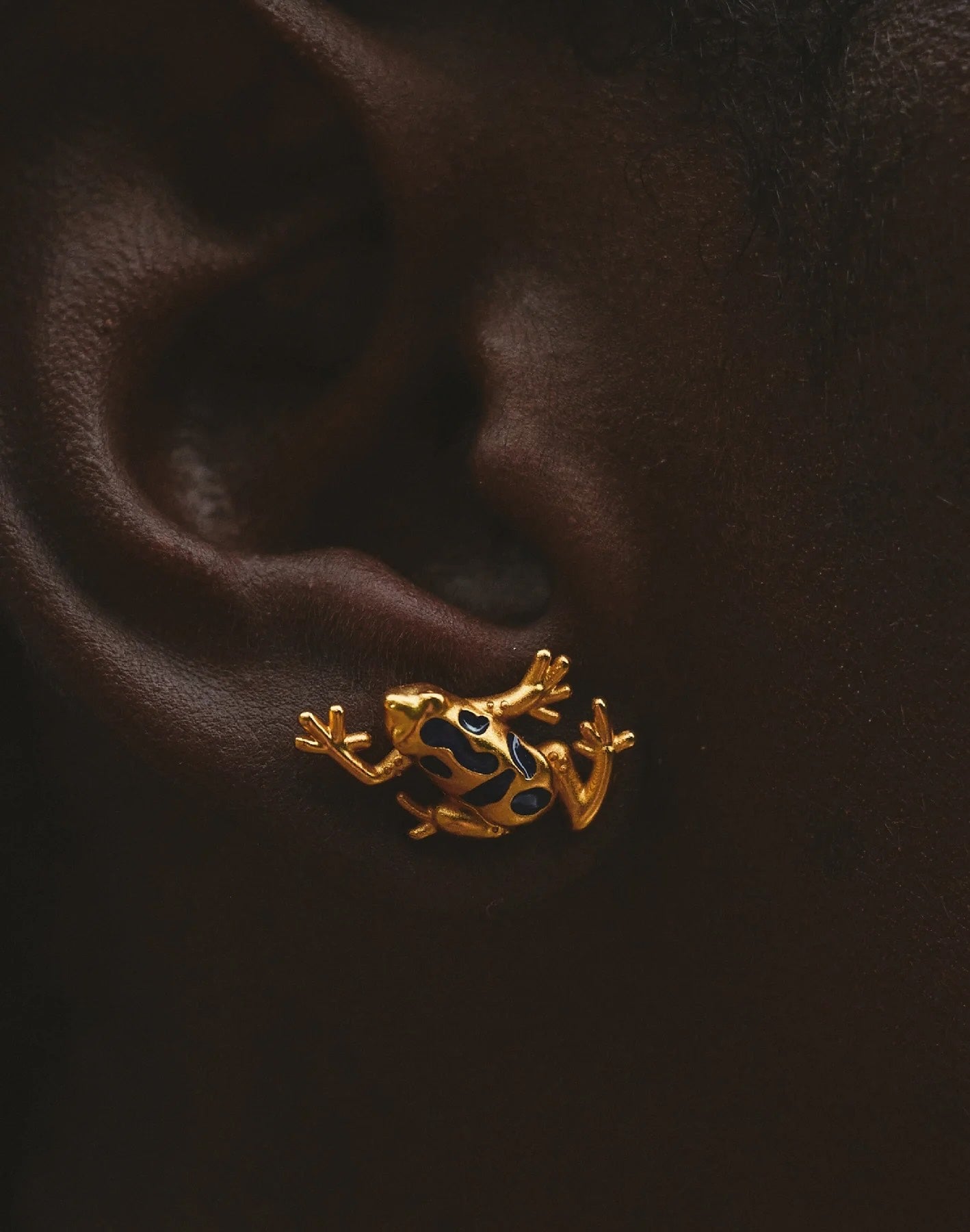 Close up of gold frog-shaped earring worn on an ear.