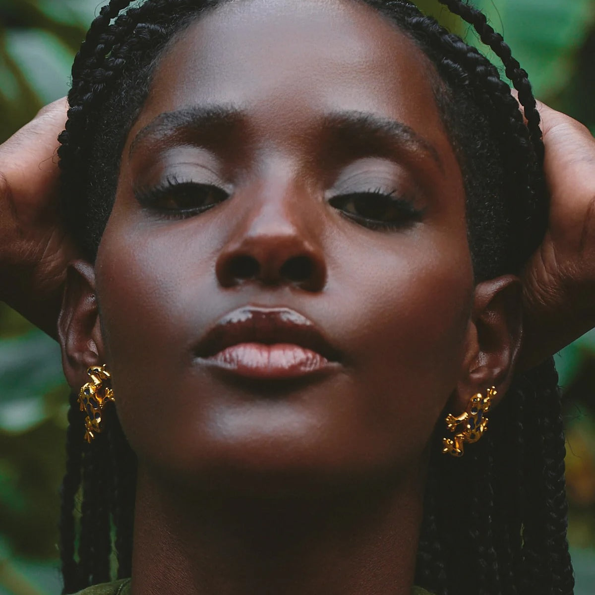 Woman with braided hair wearing gold frog earrings against a natural background