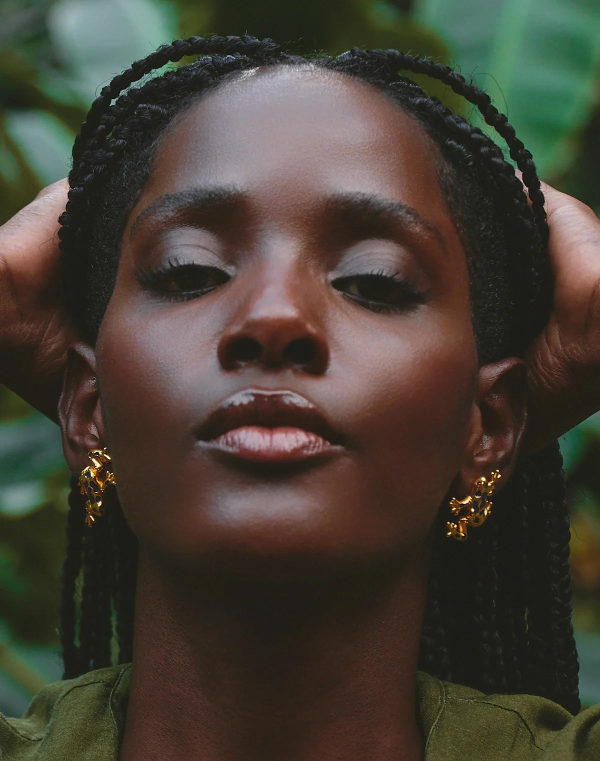 Woman with braided hair wearing gold frog earrings against a natural background