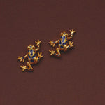 Gold plated blue enamel frog stud earrings on burgundy background